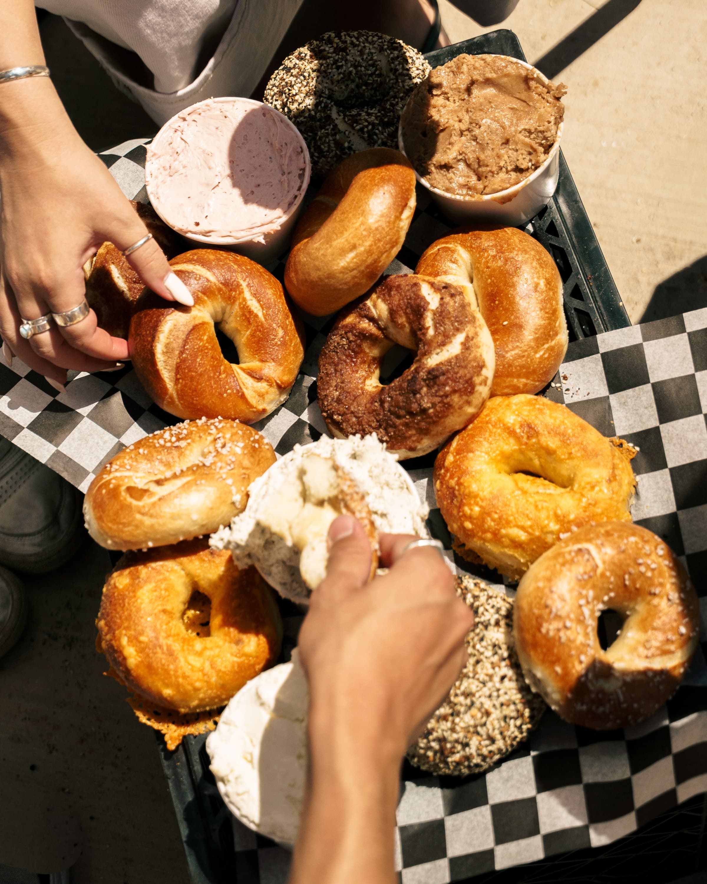Hands reaching for a spread of bagels and schmears