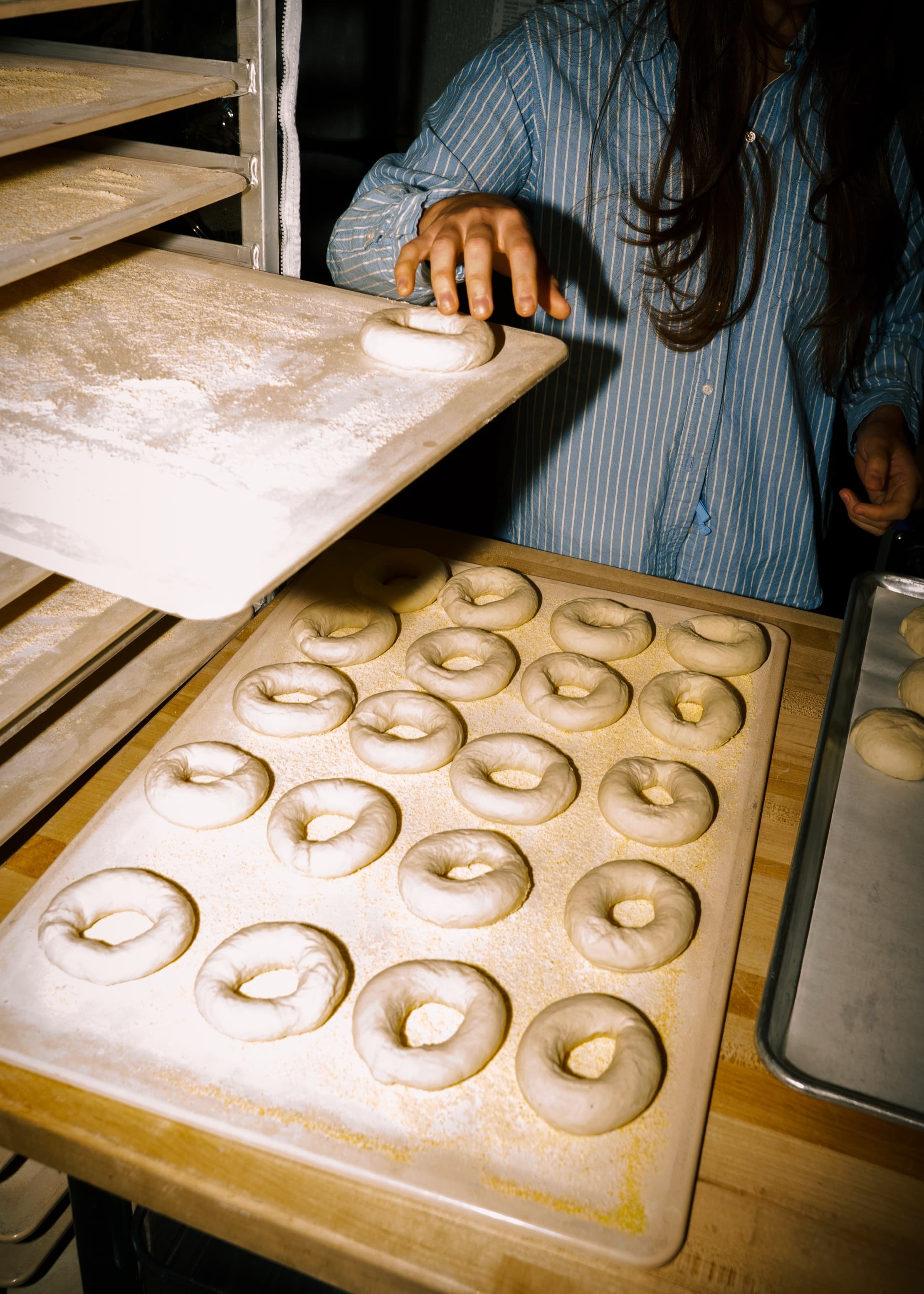 A baker placing freshly rolled bagel dough onto a tray